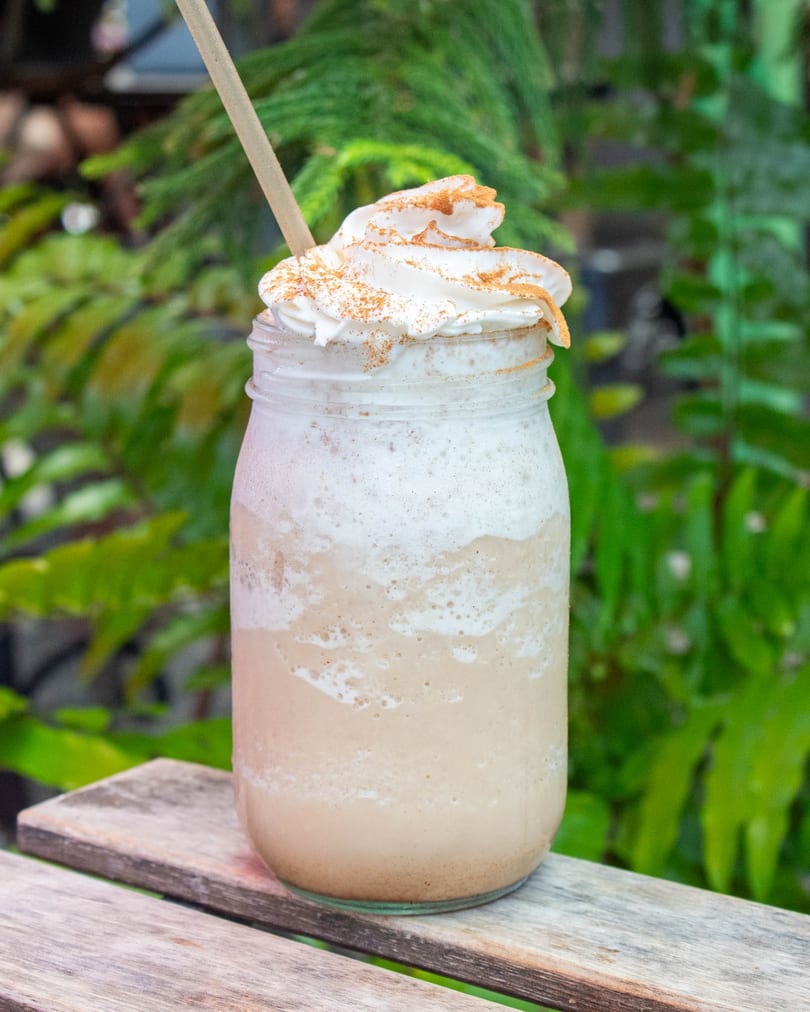A creamy blended drink with whipped cream and cinnamon in a mason jar on a wooden surface.
