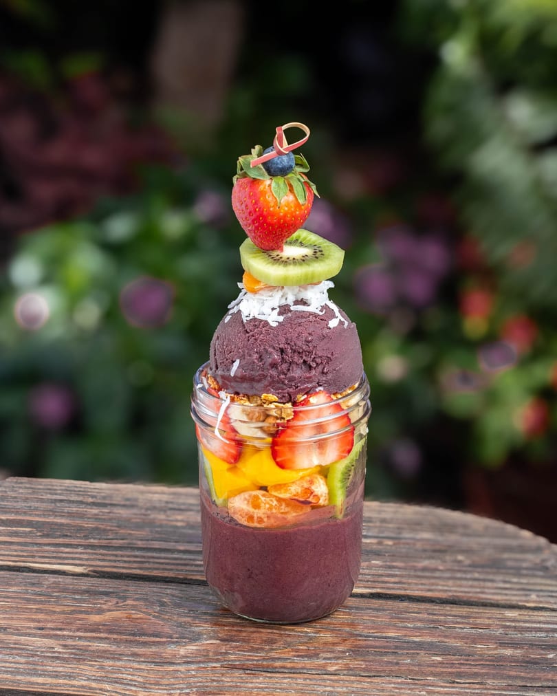 A vibrant acai bowl in a glass jar, topped with fresh fruit, granola, and coconut flakes.