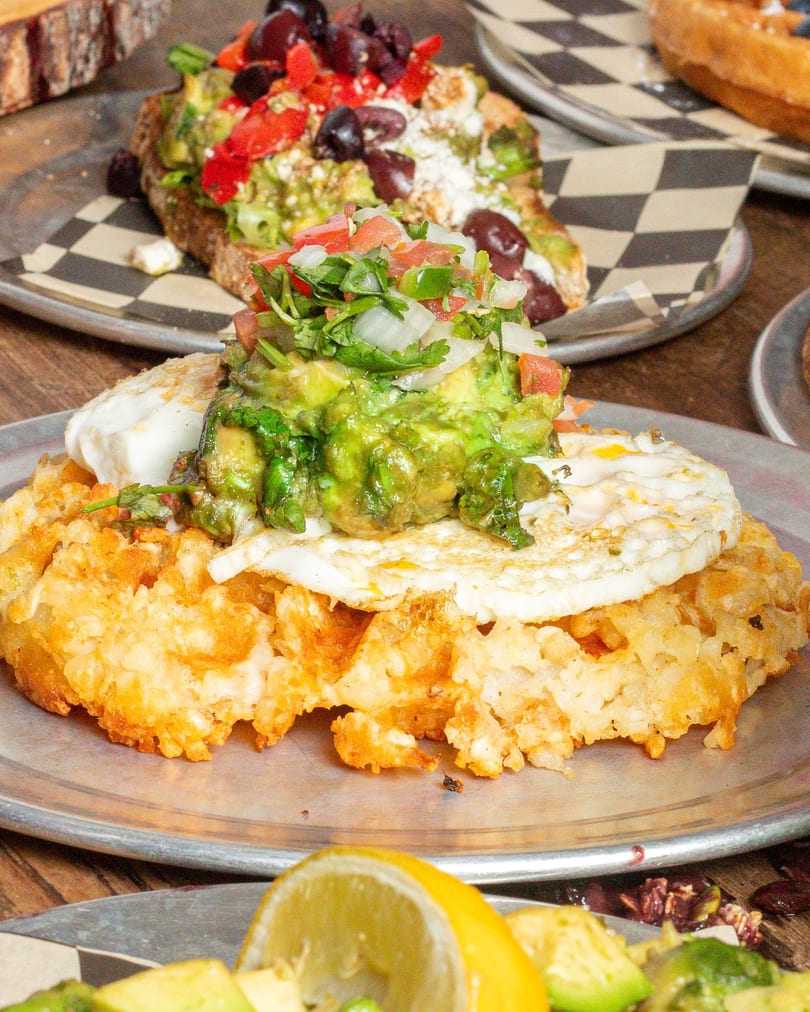 Hash brown waffle topped with a fried egg, guacamole, and pico de gallo.