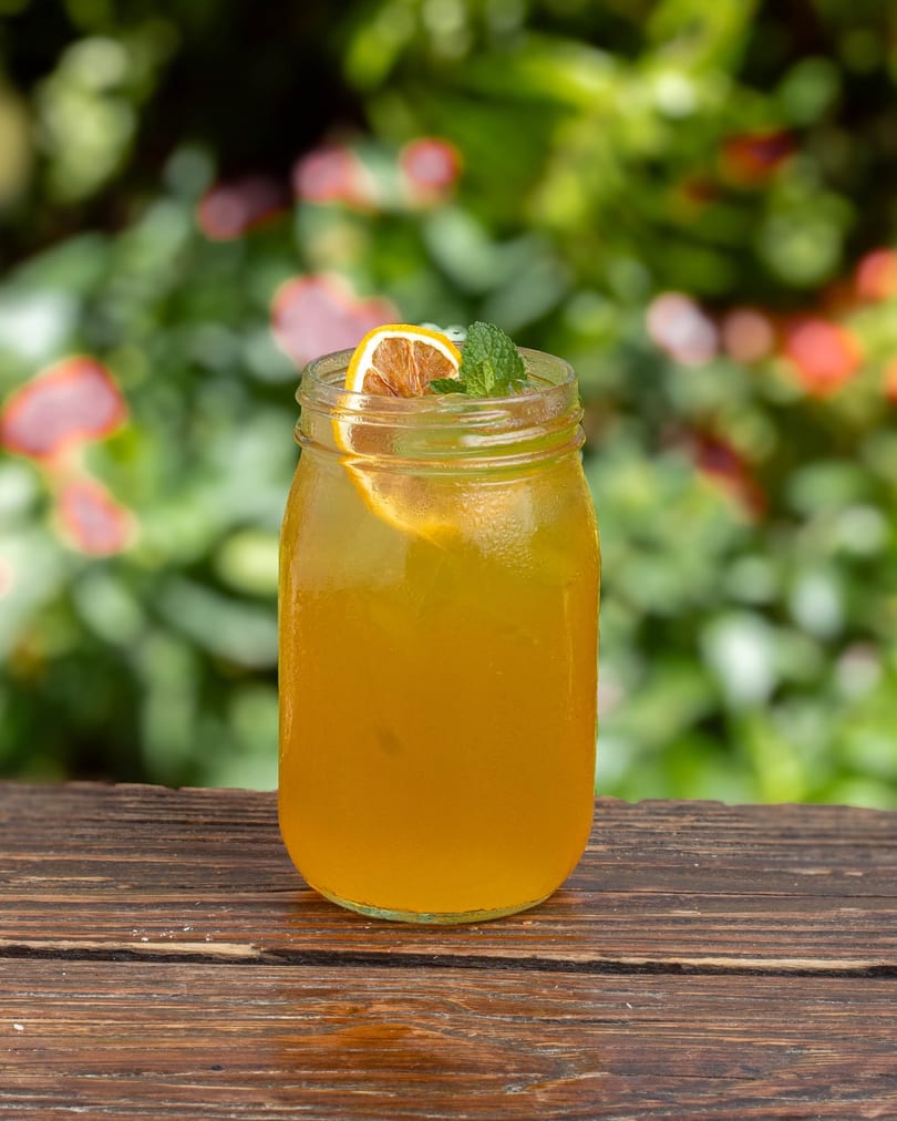 Iced tea in a mason jar with a lemon slice and mint sprig on a wooden table.