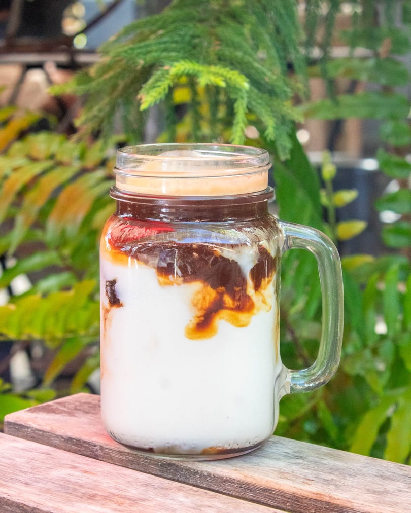 Iced coffee with milk and chocolate syrup in a mason jar on a wooden table.