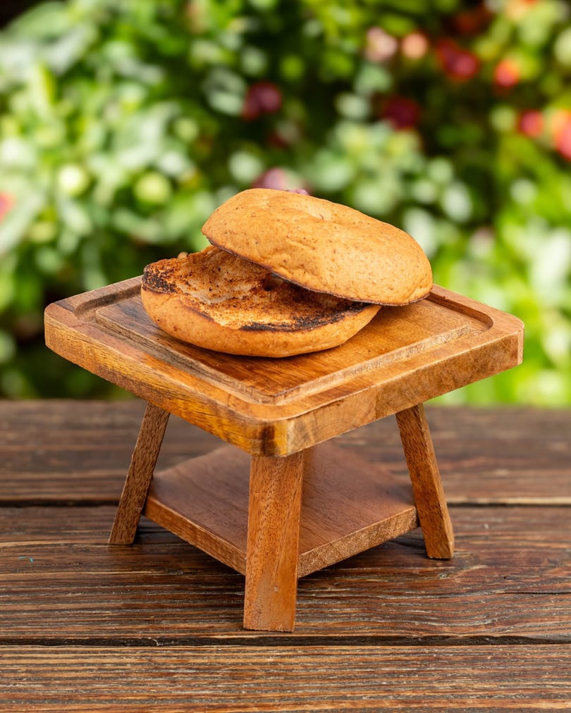 Toasted burger bun halves on a small wooden serving stand, with a blurred green background.