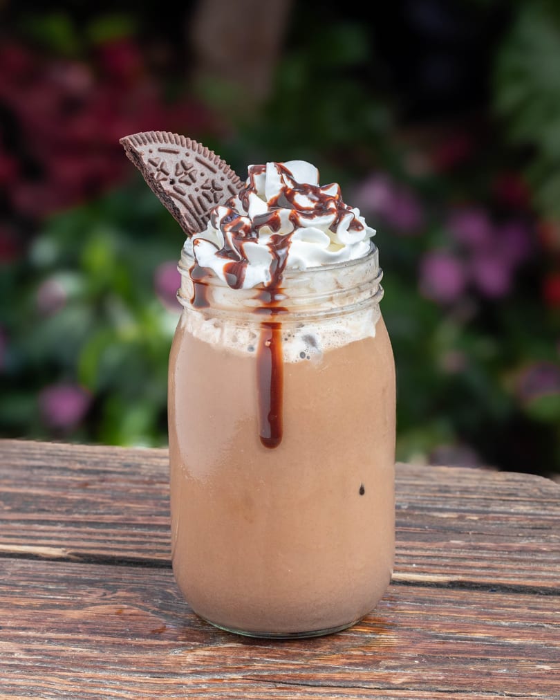 Chocolate milkshake in a mason jar, topped with whipped cream, chocolate drizzle, and a cookie.
